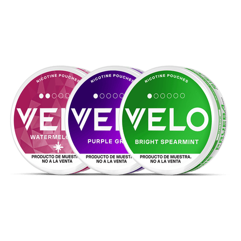 Tres envases redondos VELO Mini Trial -Sandía (rosa), Purple Grape (morado) y Bright Spearmint (verde)- expuestos uno al lado del otro. Text in English indicates that are tobaccoless samples, not for the sale.