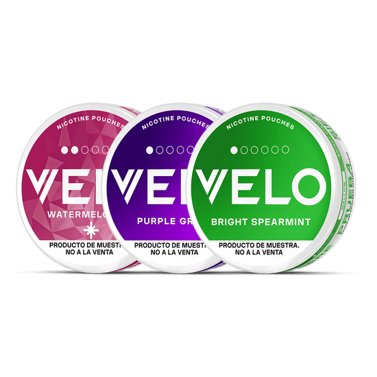 Tres envases redondos VELO Mini Trial -Sandía (rosa), Purple Grape (morado) y Bright Spearmint (verde)- expuestos uno al lado del otro. Text in English indicates that are tobaccoless samples, not for the sale.