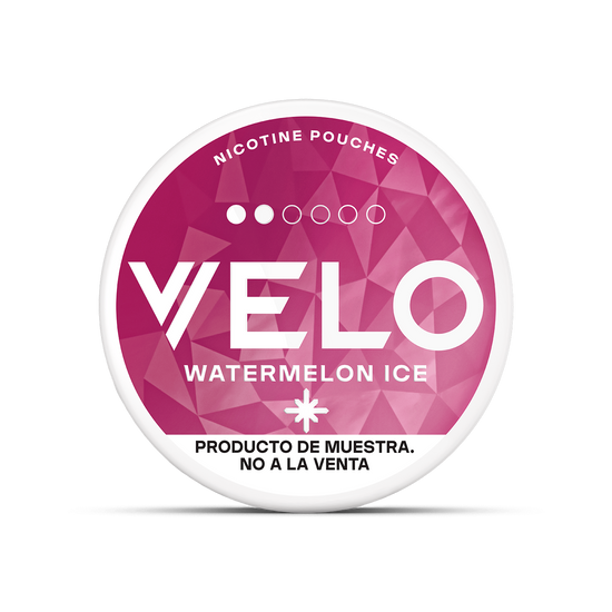 Envase redondo con motivo geométrico rosa, etiquetado VELO Mini Trial bolsas de nicotina sin tabaco. Texto en la parte inferior: PRODUCTO DE MUESTRA. NO A LA VENTA (producto de muestra, no a la venta). Marca: VELO.