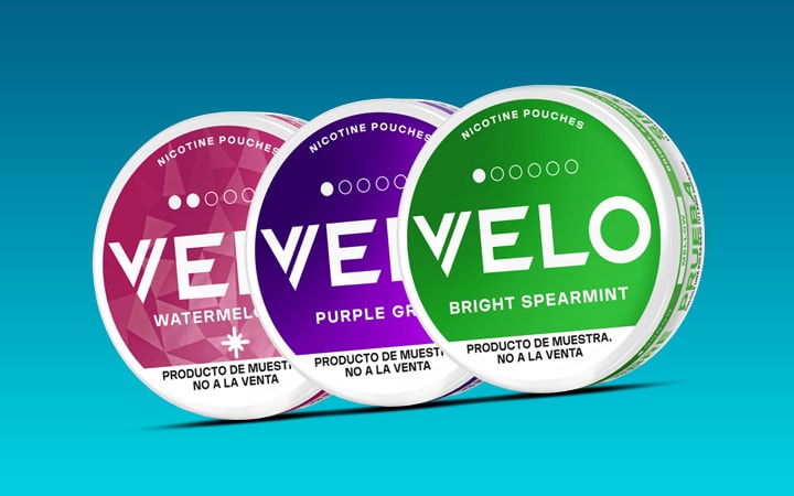 Se muestran tres envases circulares de nicotina VELO: uno rosa con la etiqueta Sandía, uno morado con la etiqueta Uva Morada y uno verde con la etiqueta Menta Verde Brillante, sobre un fondo azul degradado.