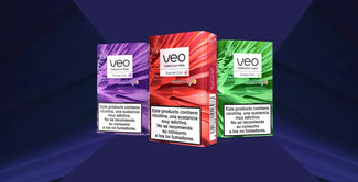 Tres cajas de productos sin tabaco Veo -morada, roja y verde- se muestran una al lado de la otra sobre un fondo geométrico morado. Cada caja lleva una etiqueta de advertencia de nicotina en español.