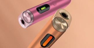 Dos elegantes aparatos electrónicos, uno rosa y otro bronce, con pantallas digitales, botones y diales giratorios, flotan sobre un fondo beige claro.
