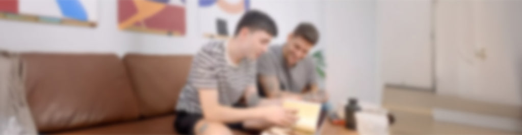 Dos personas están sentadas en el sofá de un salón, mirando juntas un libro abierto. La imagen está intencionadamente borrosa, lo que hace que los detalles y los rasgos faciales sean poco claros.