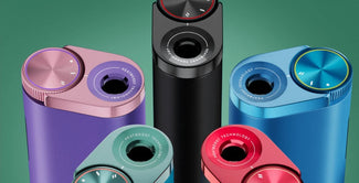 Varios dispositivos cilíndricos de colores con acabados metálicos y grandes esferas redondas están dispuestos en posición vertical sobre un fondo verde. Los aparatos son de color morado, rosa, negro, azul y rojo, y llevan la etiqueta HEATBOOST TECHNOLOGY.